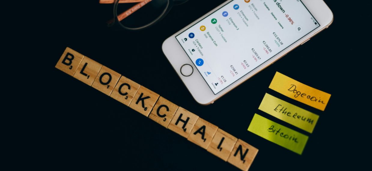 a smartphone,pair of glasses, sticky notes and scrabble on tiles that spell blockchain